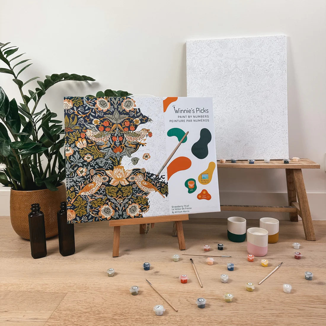 Paint by Number Strawberry Thief kit showing fabric-inspired birds, strawberries, paints, brushes, and canvas on wooden table.