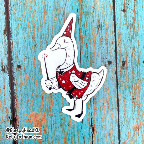 Wizard Duck Sticker featuring a white duck in a red wizard hat and robe holding a magic wand on wood background.