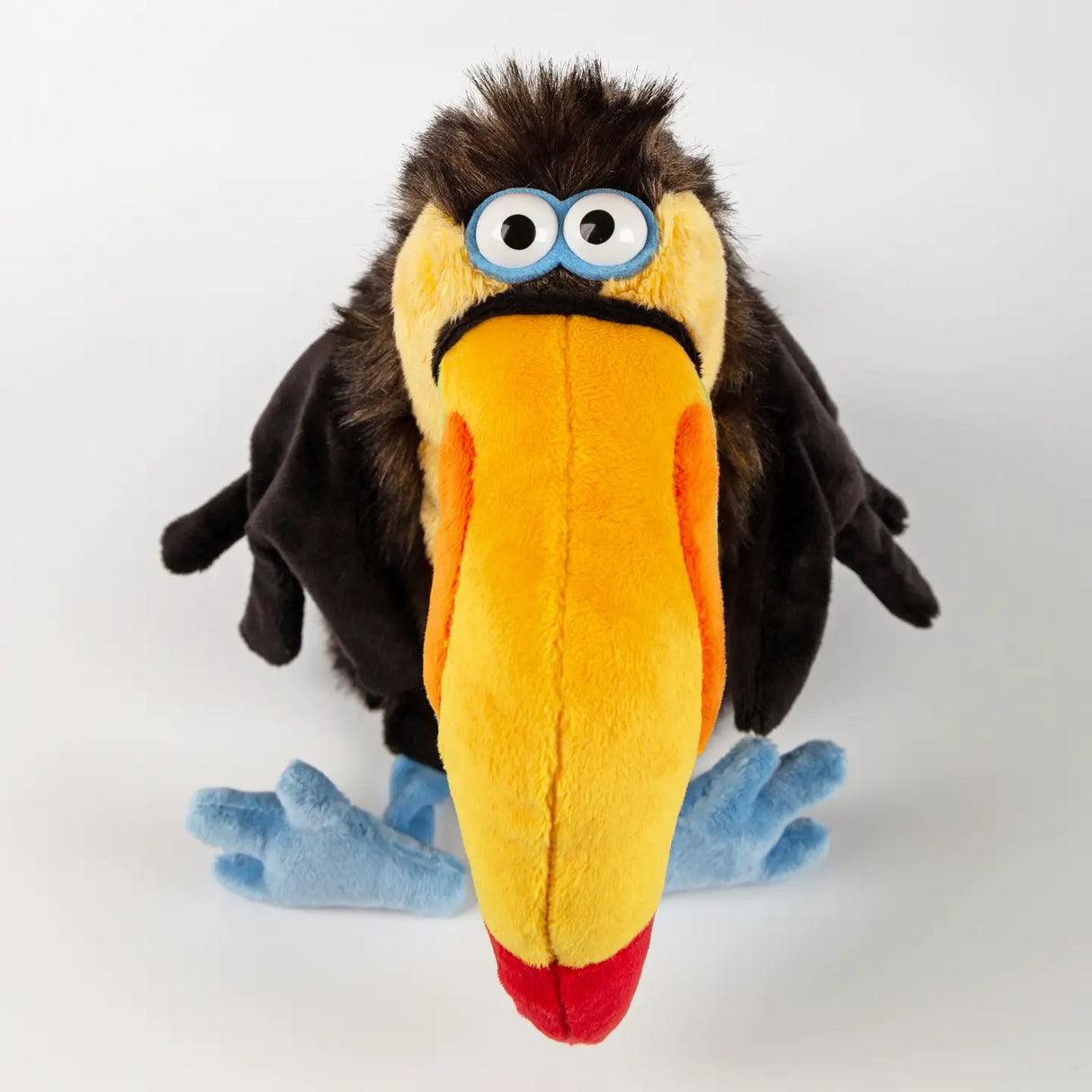 Chakka Tukan Toucan plush with large yellow beak, blue feet, and wide eyes, looking anxious and adorable.