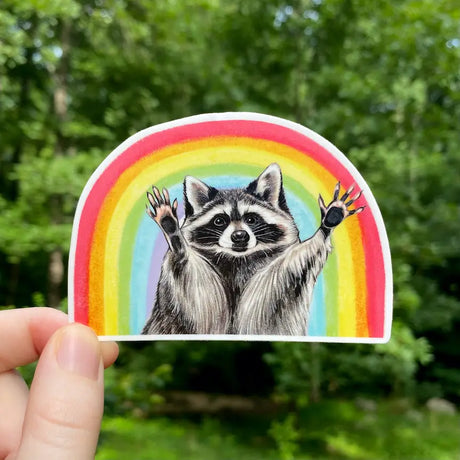 Rainbow Raccoon Sticker showing a cute raccoon with raised paws inside a colorful rainbow arch on vinyl material.