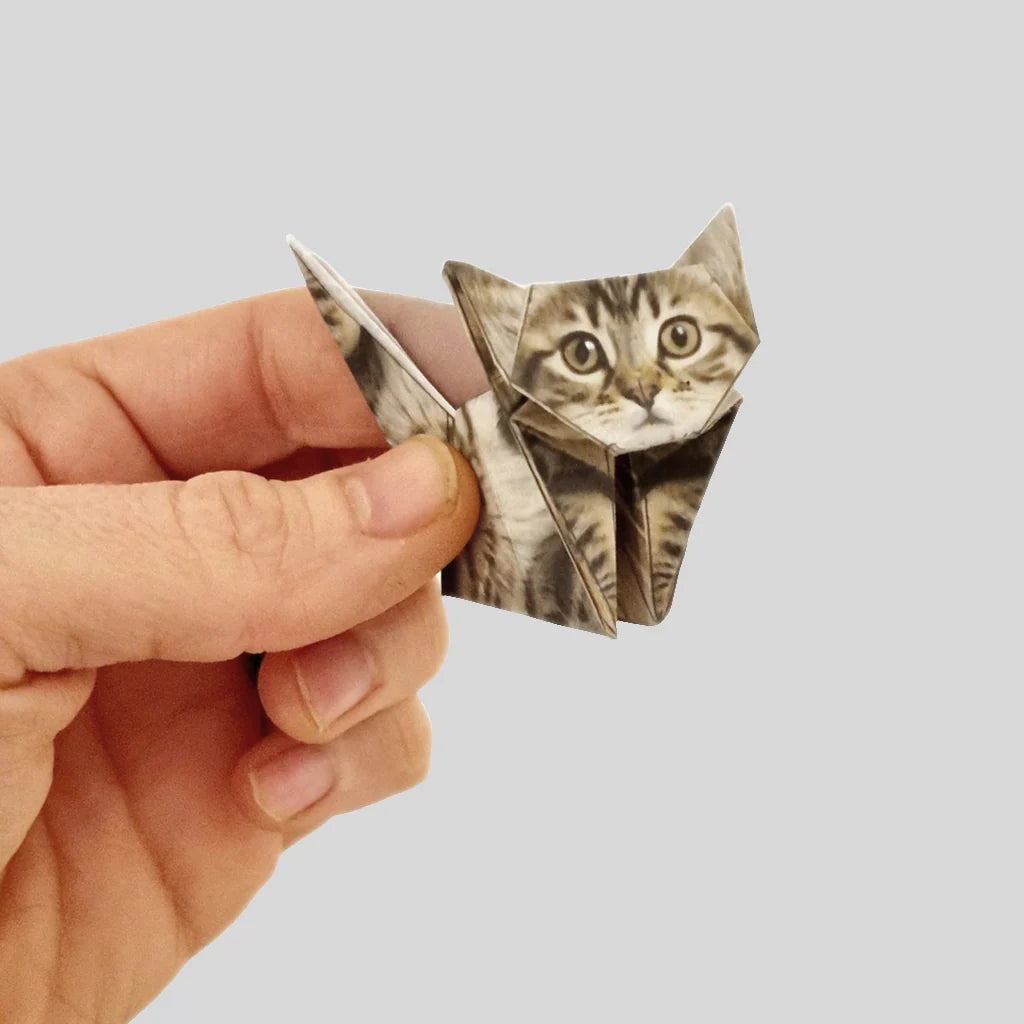 Hand holding a small origami cat with a realistic tabby cat print on eco-friendly paper against a gray background