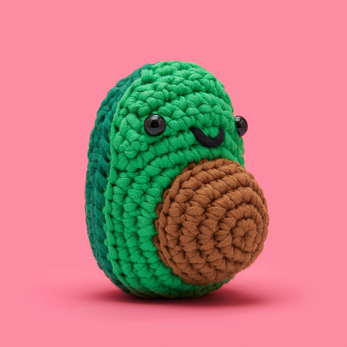 The Woobles Crochet Kit | Mateo the Avocado showing a cute green crocheted avocado with big eyes and brown seed on pink background