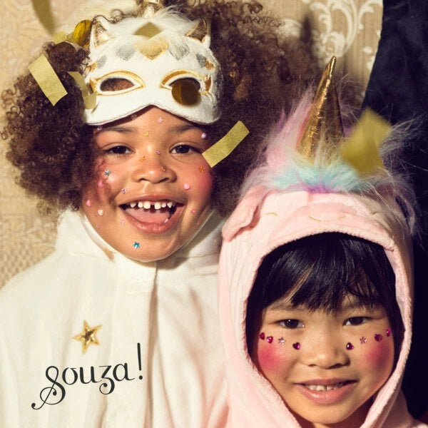 Two children wearing unicorn-themed masks with golden horns and decorative face stickers smiling happily