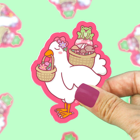 Hand holding a colorful Picnic Chicken Sticker featuring a chicken with baskets of wildflowers and mushrooms.