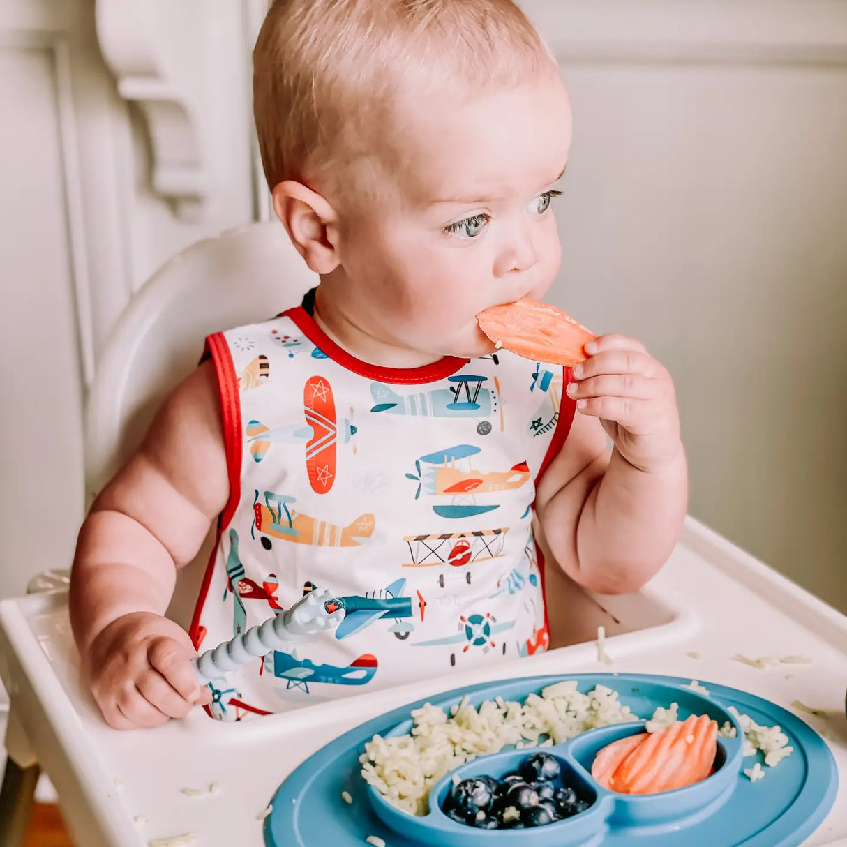 Baby wearing Bapron | Retro Airplanes 6M-3T bib-apron while eating, featuring full-coverage, waterproof fabric design.