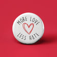 Button | More Love Less Hate white button with red heart and black text on red background, 1.25 inches expressing positivity and kindness.