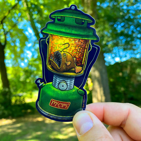 Anglerfish Lantern Sticker showing a vibrant green lantern with a glittering anglerfish inside held outdoors in natural light.