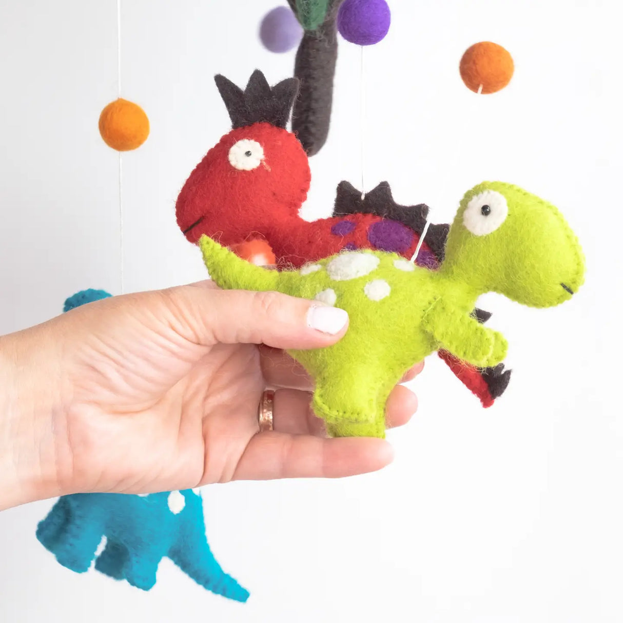 Hand holding Felt Mobile | Dinosaur with colorful wool dinosaurs hanging against a white background.