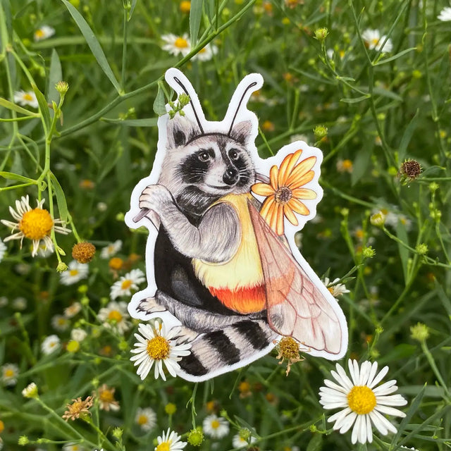 Bumblebee Raccoon Sticker featuring a raccoon dressed as a bumblebee holding a yellow flower on green foliage background.