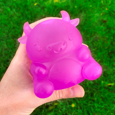 Hand holding a bright purple Super Duper Sugar Squisher Cow squish toy with a gooey center on green grass background