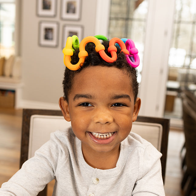Smiling child wearing colorful Plip Links on their head showing creative and sensory fun with silicone link halves.