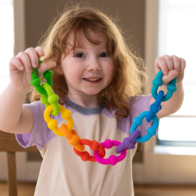 Child holding a colorful rainbow chain made of Plip Links silicone construction and fidget toy pieces.