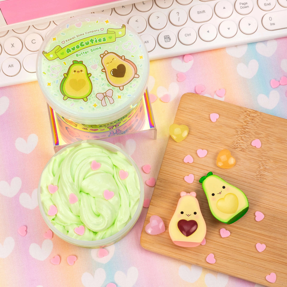 AvoCuties Butter Slime with light green creamy texture and cute avocado couple charm on pastel heart background.