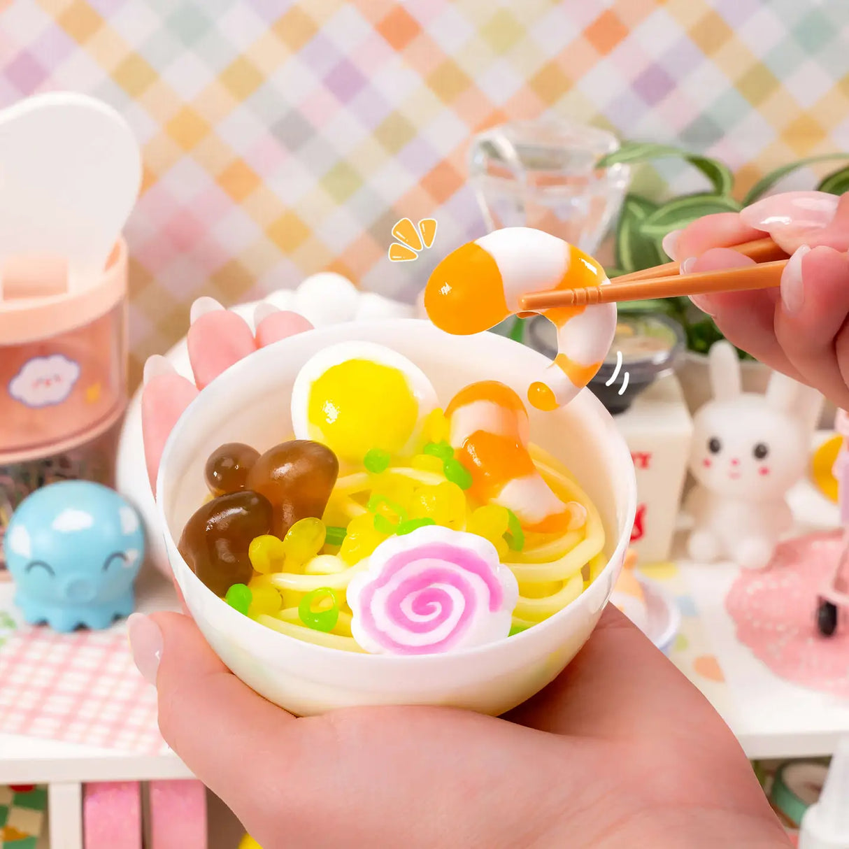 Hands holding a bowl of Instant Ramen Noodles Slime Kit with colorful slime noodles and garnishes being picked up with chopsticks.