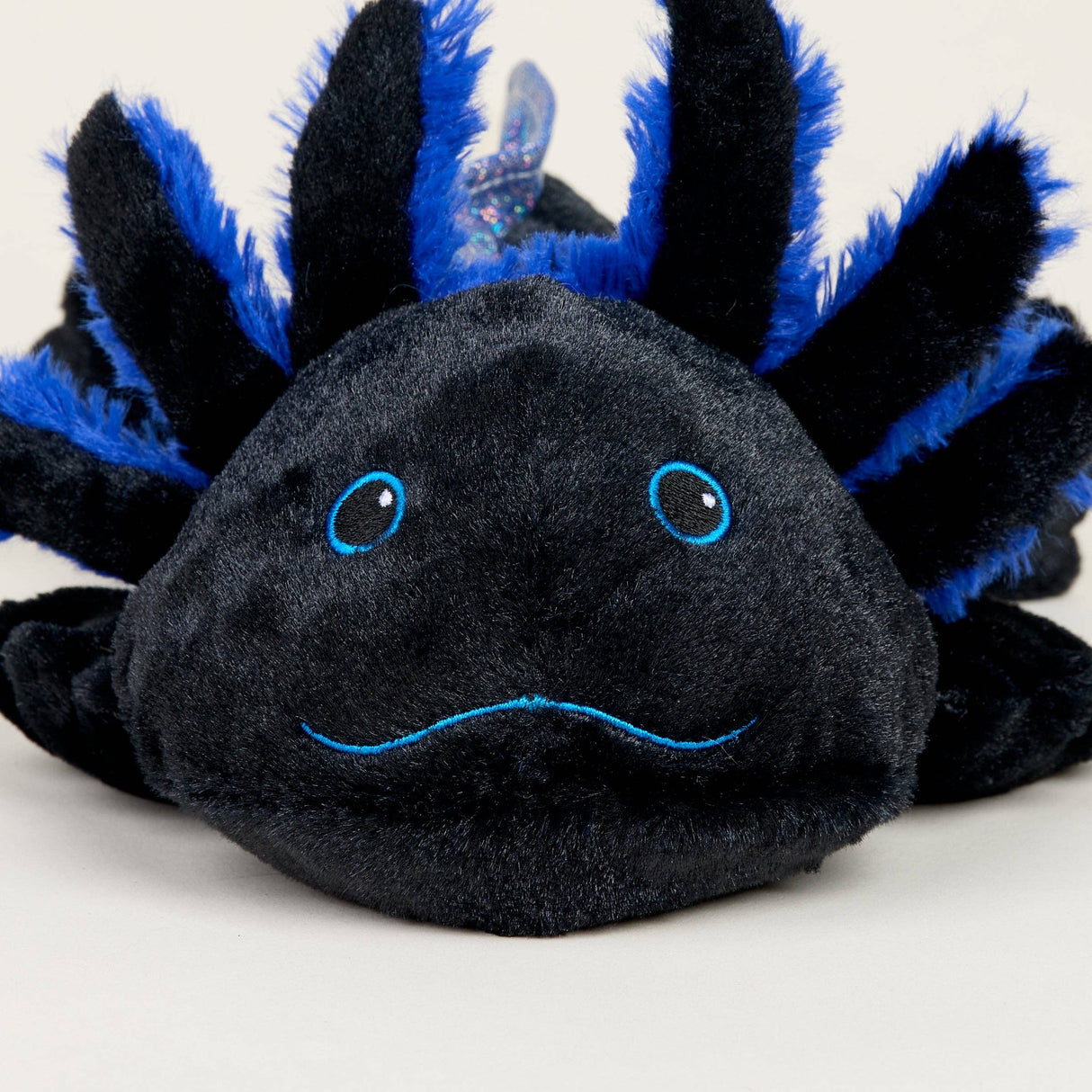 Close-up of a soft black and blue axolotl plush toy with embroidered facial features and fluffy gills