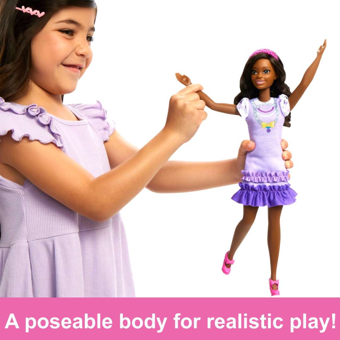 Child playing with My First Barbie Black Hair doll wearing a lilac dress and pink shoes, featuring a poseable body.