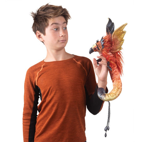 Boy wearing an orange shirt holding a colorful Phoenix Wristlet finger puppet with plush flames and movable head.