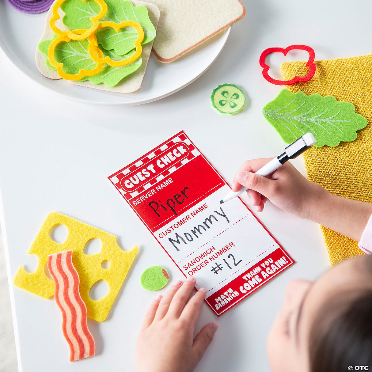 Child writing order on red guest check from Math Sandwich felt food playset with sandwich ingredients on table