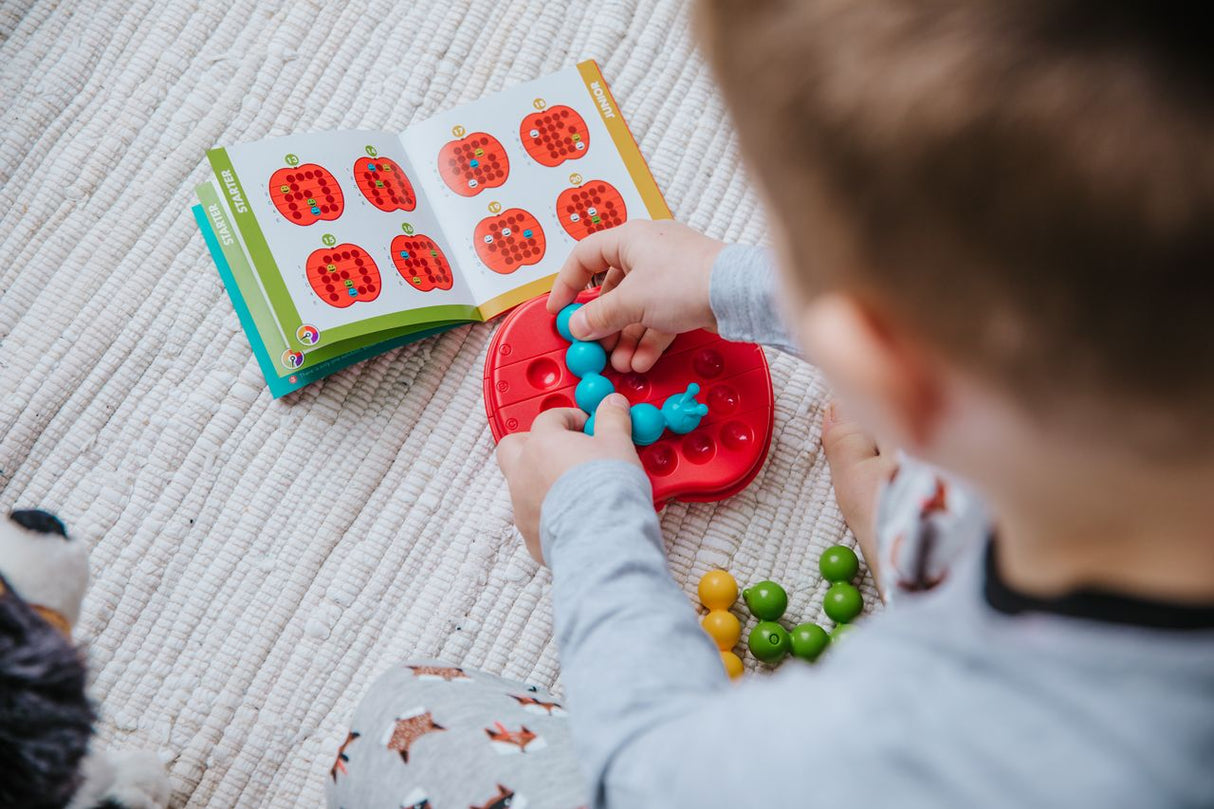 Child playing Apple Twist puzzle game with colorful caterpillars and twistable game board on carpet.