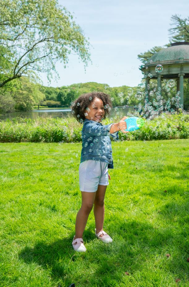 Child outdoors happily using the Fubbles | Bubble Surge Mini Blaster to create bubbles in a sunny park.