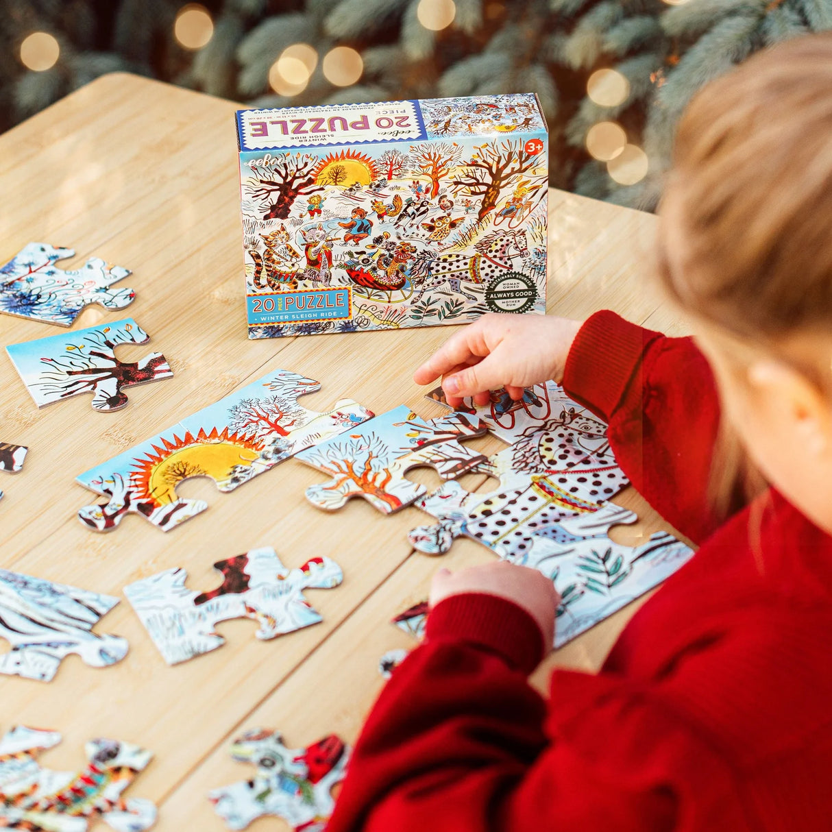 Child assembling a colorful 20-piece winter sleigh ride puzzle with detailed animal illustrations on a wooden table.