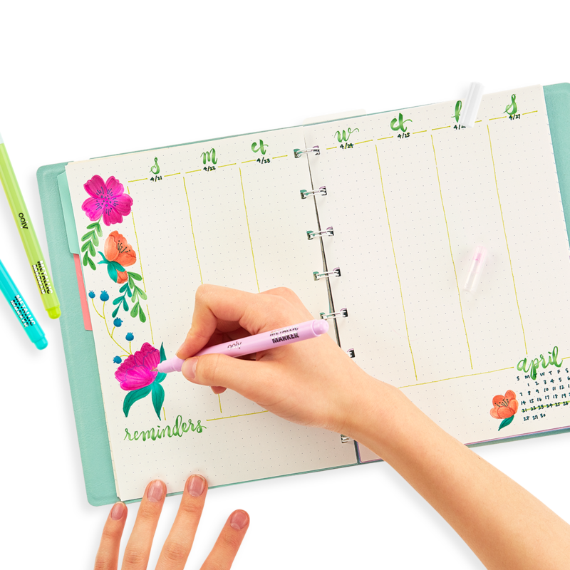 A hand using Color Lustre Metallic Brush Markers to add bright, shimmering floral designs and reminders in a planner.