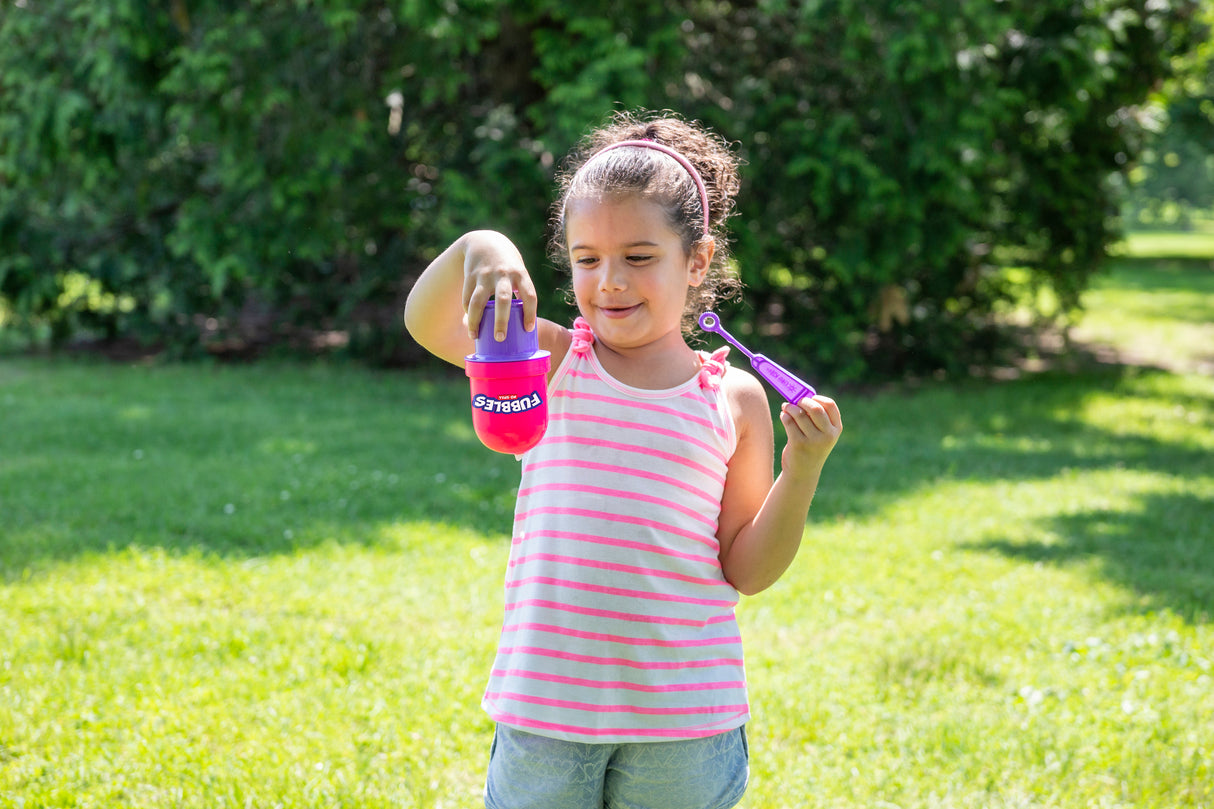 Child playing outdoors with the Fubbles | No-Spill Bubble Tumbler holding bubble wand and tumbler upside down.