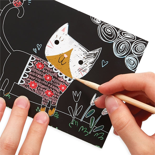 Scratch & Scribble Cutie Cats showing hands using wooden stylus to reveal colorful cat design on mini scratch art card.