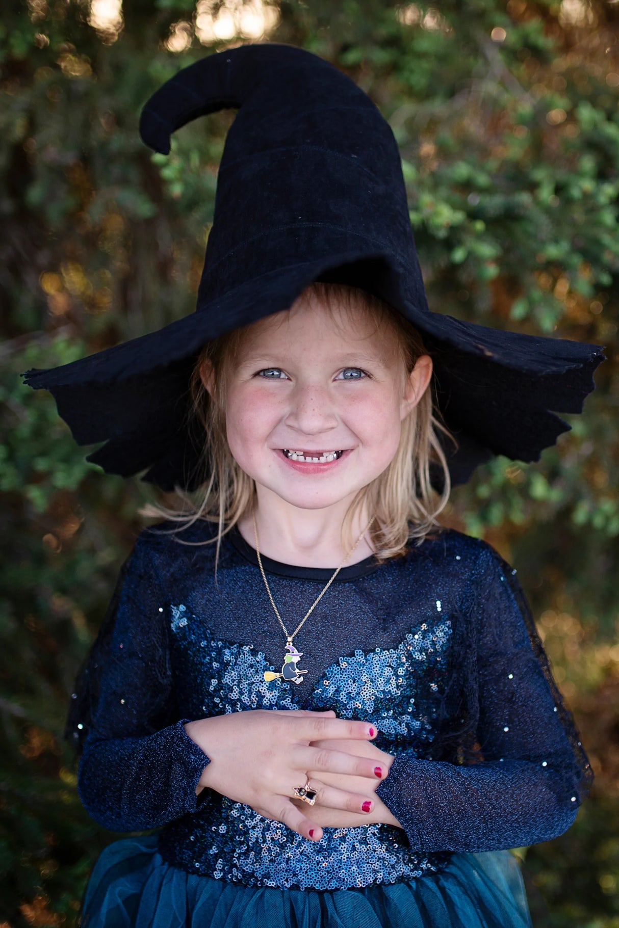 Smiling child wearing the Mighty Witch Hat, a large black witch hat perfect for spooky outfits and magical fun.
