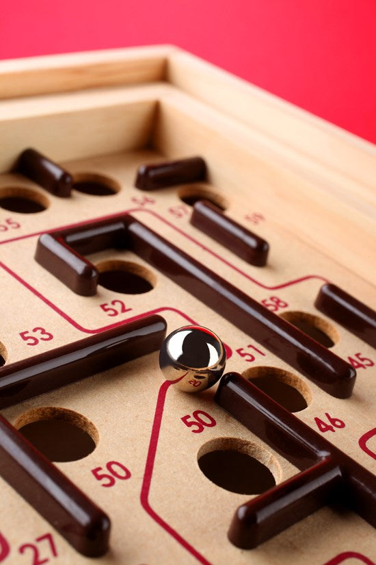 Close-up of the Labyrinth wooden game showing metal ball navigating numbered holes and obstacles on board.