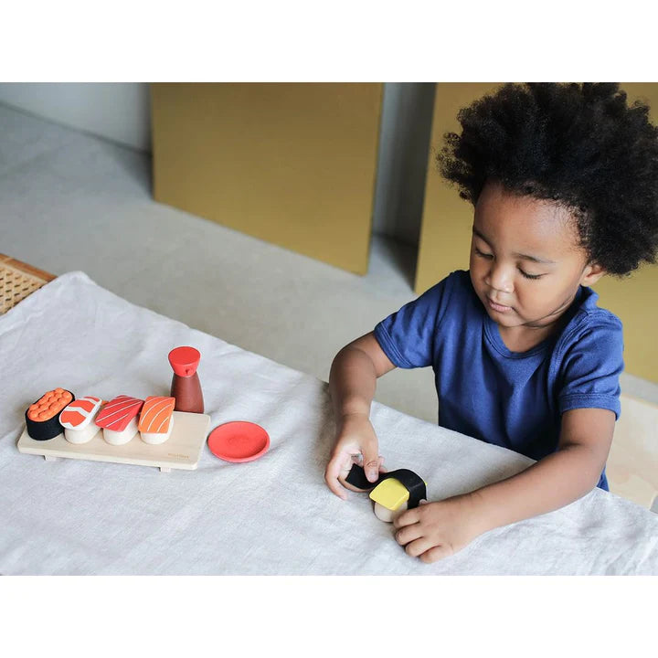 Child playing with the PlanToys Sushi Set including sushi pieces, tray, shoyu bottle, and sauce dish for pretend play.