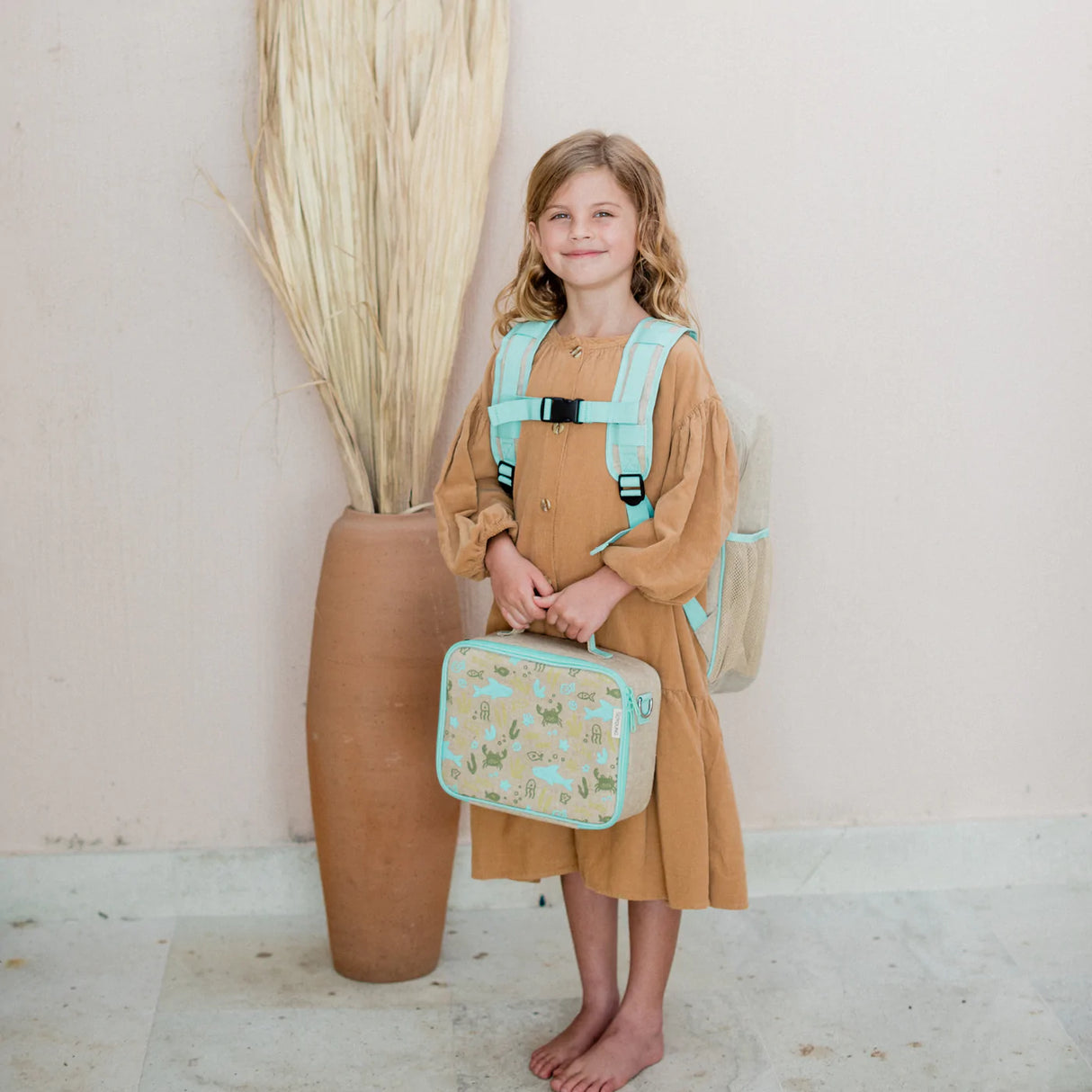 Smiling child holding Lunch Box | Under the Sea with ocean-themed print and wearing matching backpack straps
