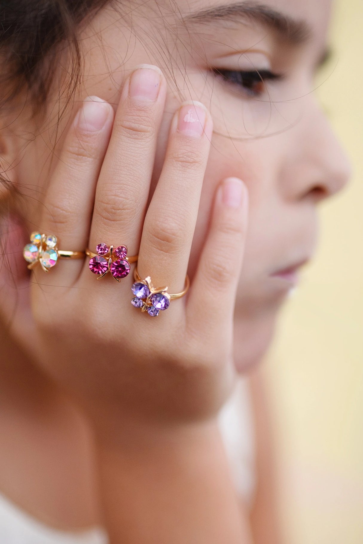 Boutique Butterfly Gem Rings on a child's hand featuring jewel-toned butterfly designs on gold bands for little fingers.