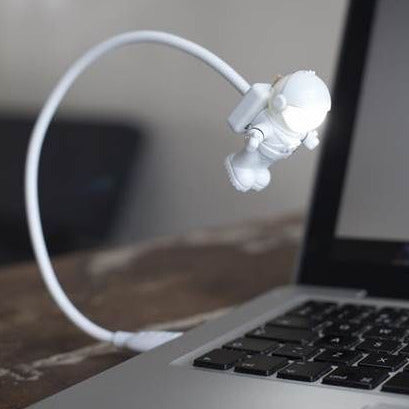 USB Astronaut Light plugged into laptop USB port with flexible arm and spaceman figure lighting the way.