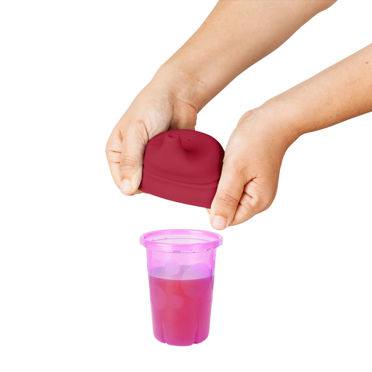 Hands stretching a SNUG Spout Sippy Lids Pinks silicone lid over a pink toddler cup filled with juice.