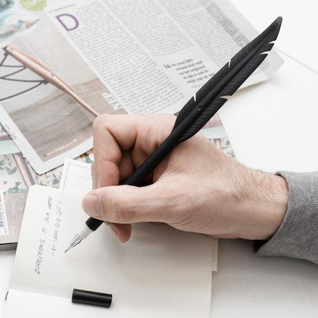 Hand holding a black Feather Pen writing on paper, showcasing the modern quill gel pen with black ink.