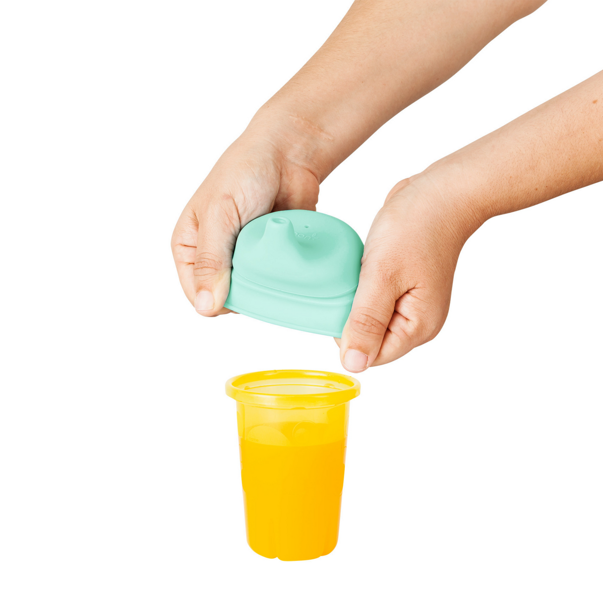 Hands placing a SNUG Spout Sippy Lids Greens silicone lid on a yellow cup to prevent spills.