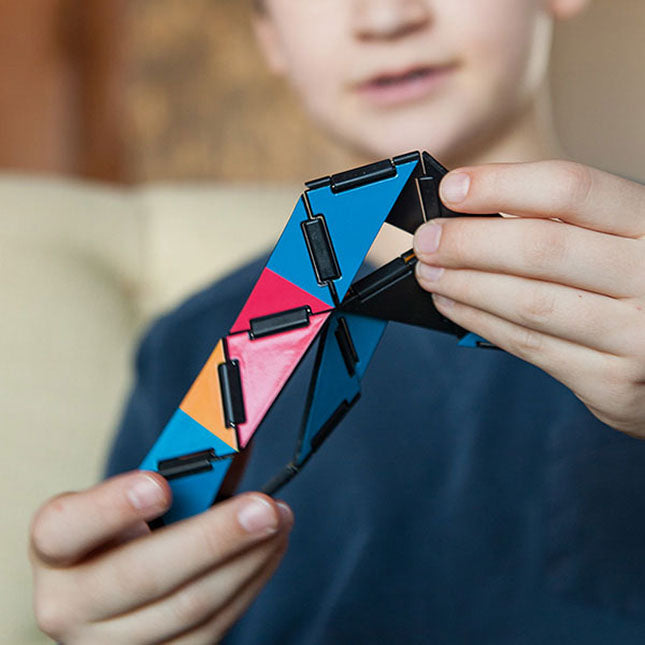 Child holding and manipulating colorful articulating Ivan's Hinge fidget toy with hinged sections and vibrant patterns.