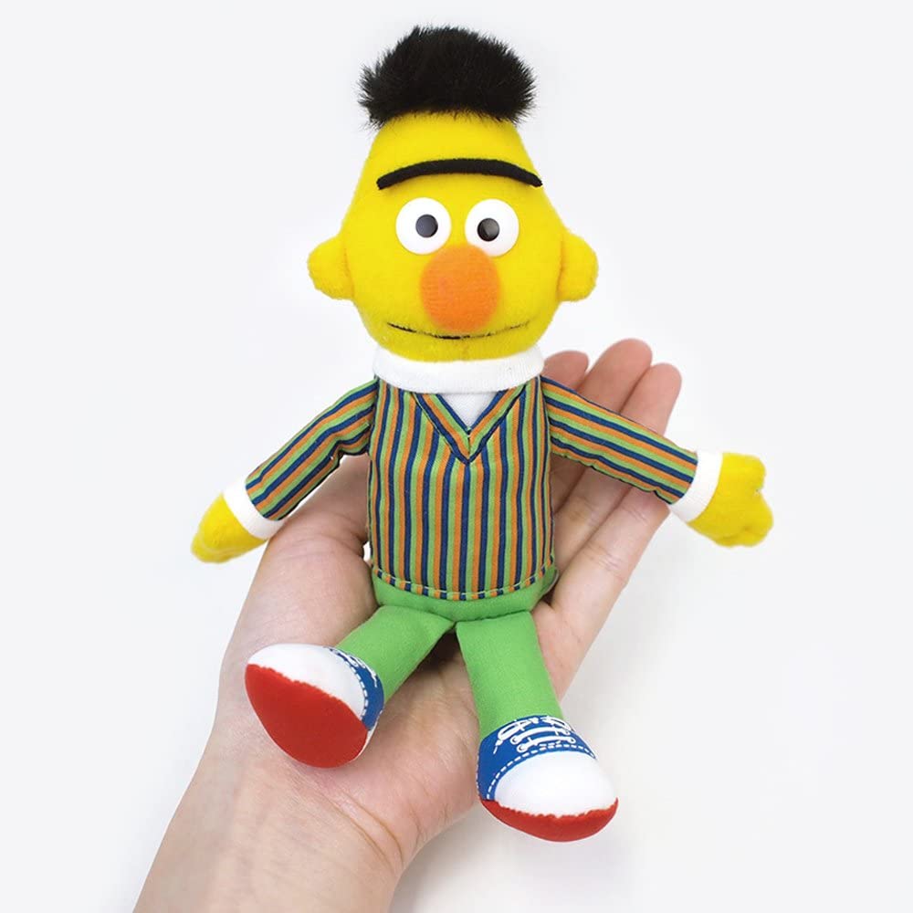 Hand holding a 7” beanbag Sesame St Character plush toy wearing striped shirt and green pants.