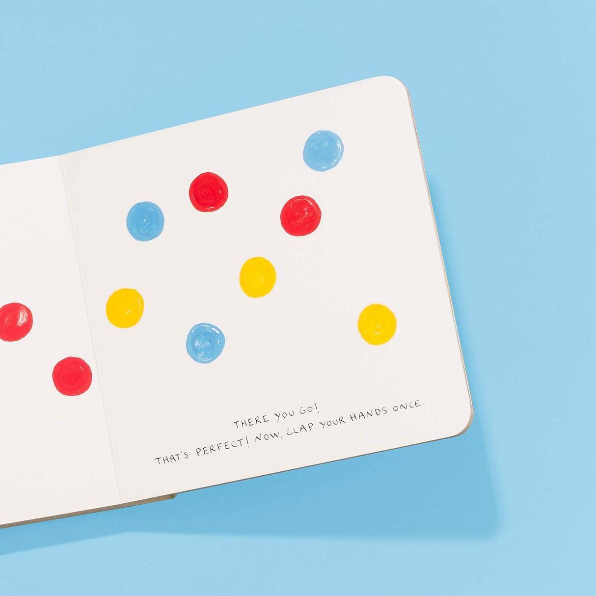 Open pages of Press Here book showing colorful red, blue, and yellow dots on white pages against a blue background