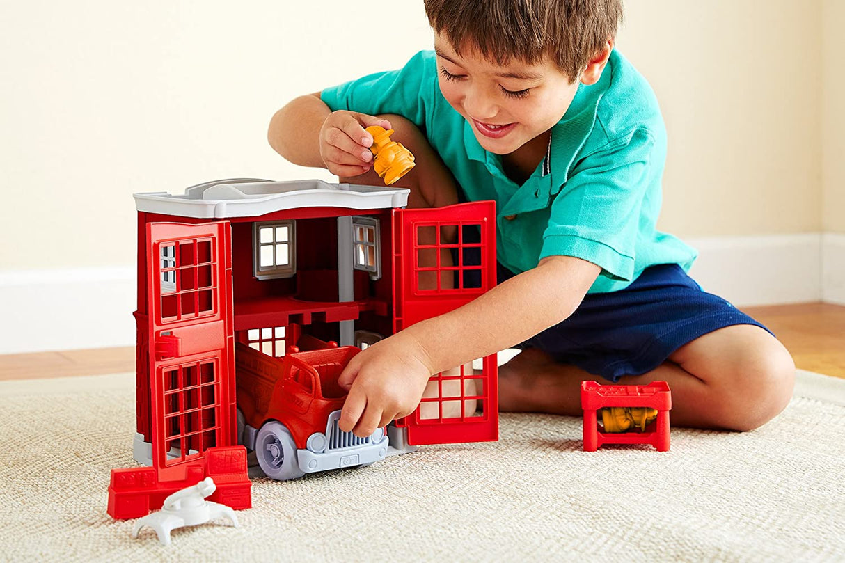 Child playing with Fire Station Play Set featuring fire engine, fire station, and firefighter cat figures indoors.