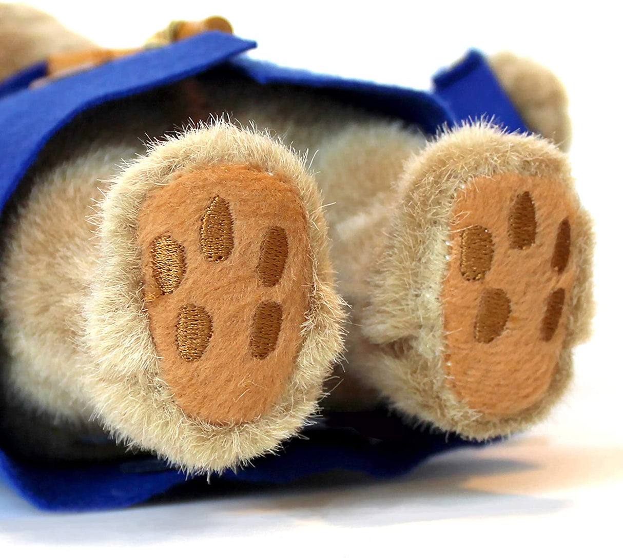 Paddington Bear plush showing soft honey brown feet with embroidered paw prints and blue coat edges.