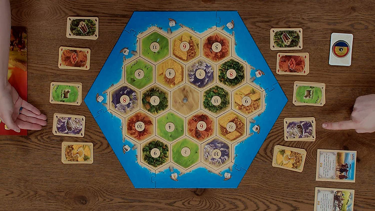 Catan Seafarers 5th Edition board game setup with hex tiles, cards, and player hands on a wooden table.