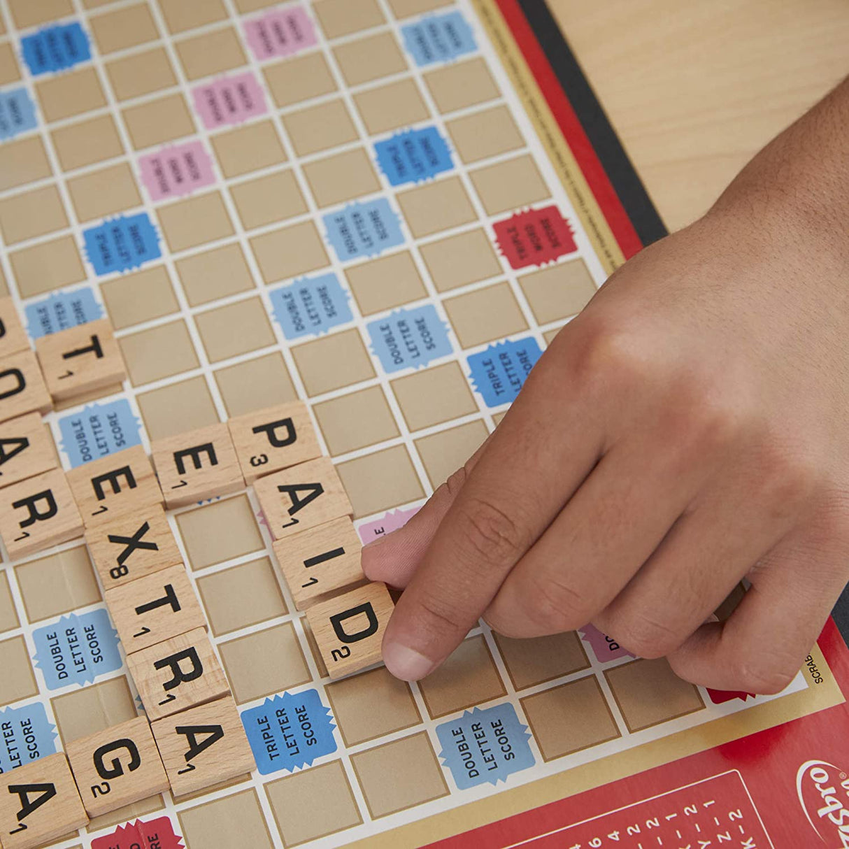 Scrabble game board with wooden letter tiles and a hand placing the word PAID in this classic Scrabble set.