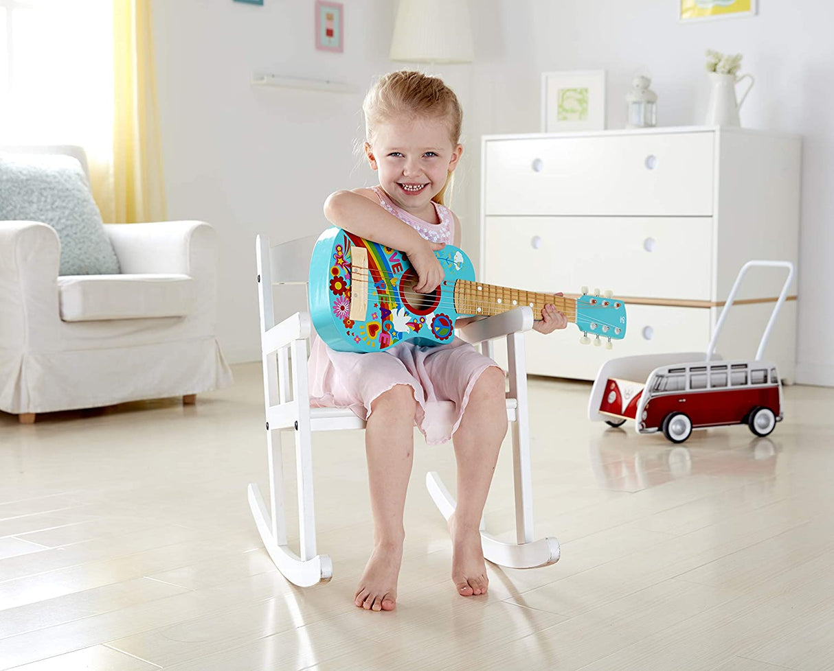 Young child sitting on chair playing the colorful 26-inch Flower Power Guitar in a bright living room.