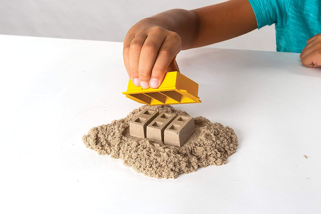 Child using brick mold with brown Kinetic Sand from Kinetic Sand Dig & Demolish playset on white surface.