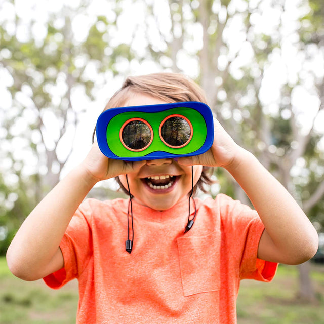 Child smiling outdoors using Kidnoculars Binoculars with bright blue and green focus-free eyepieces and neck strap.