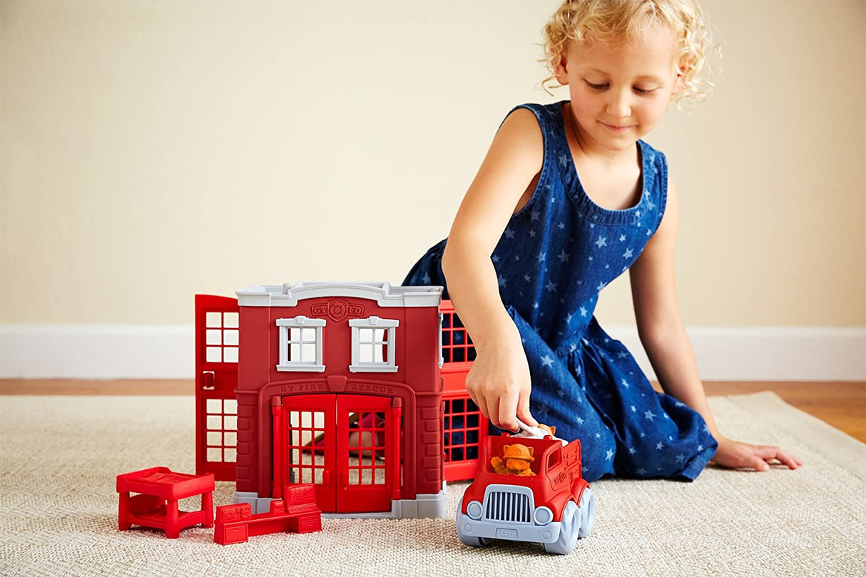 Child playing with the Fire Station Play Set featuring a red fire station and fire engine on a carpeted floor.