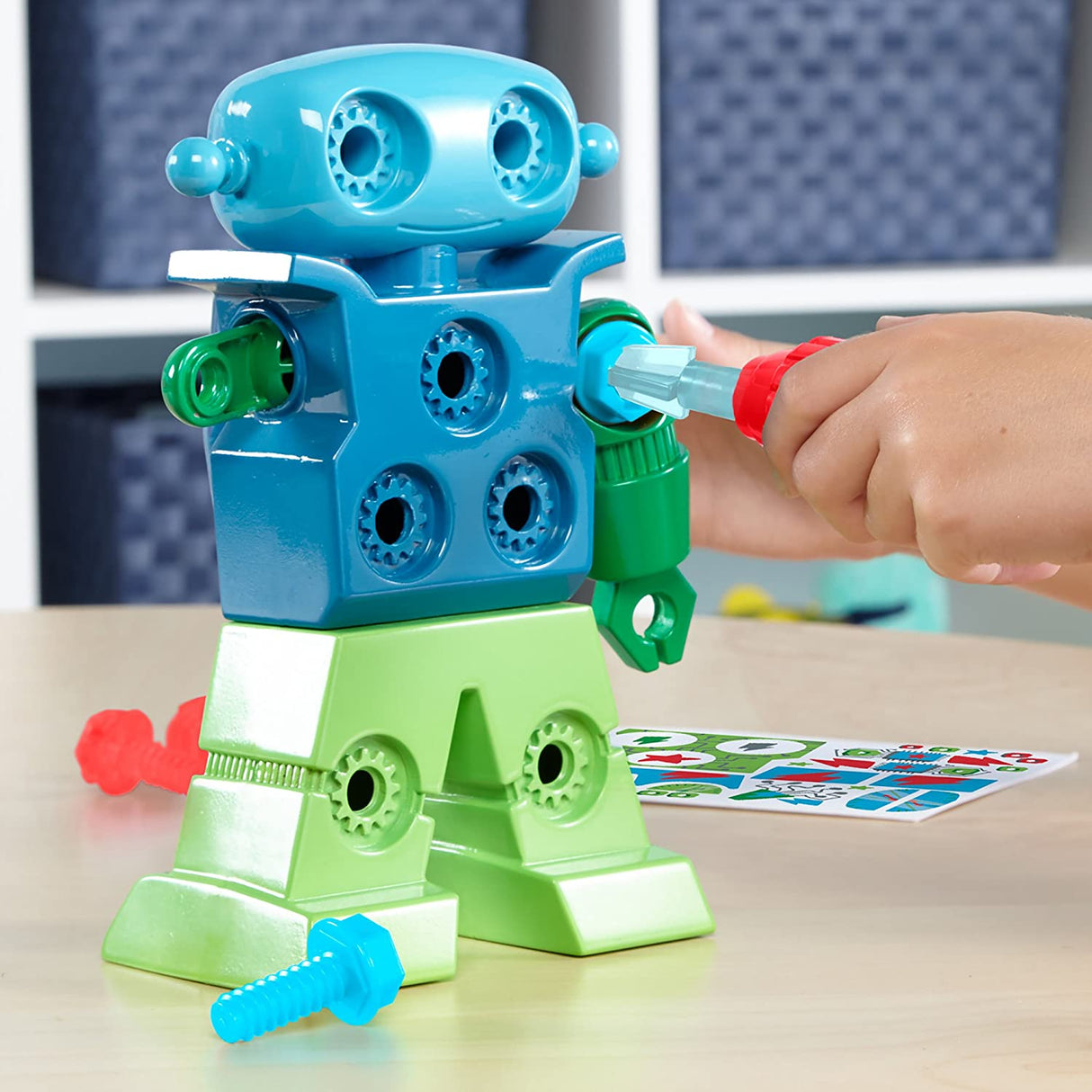 Child using a screwdriver on the Design & Drill Robot toy with colorful bolts and green and blue parts.