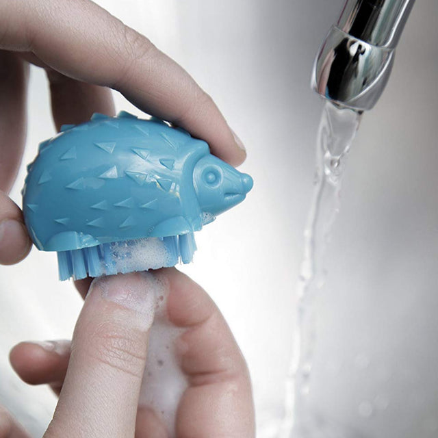 Blue Hedgehog Nail Brush with soft bristles cleaning under fingernail, held under running water.